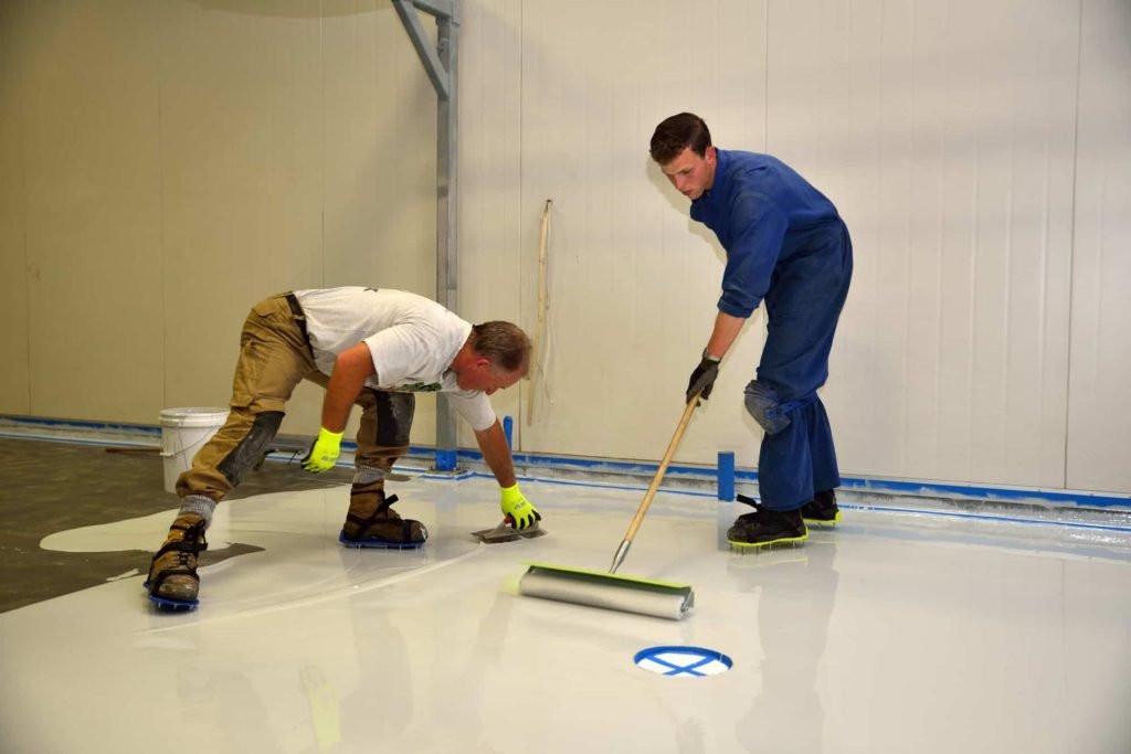 Two men using rollers to paint a white floor, representing epoxy flooring services in Fresno, CA.
