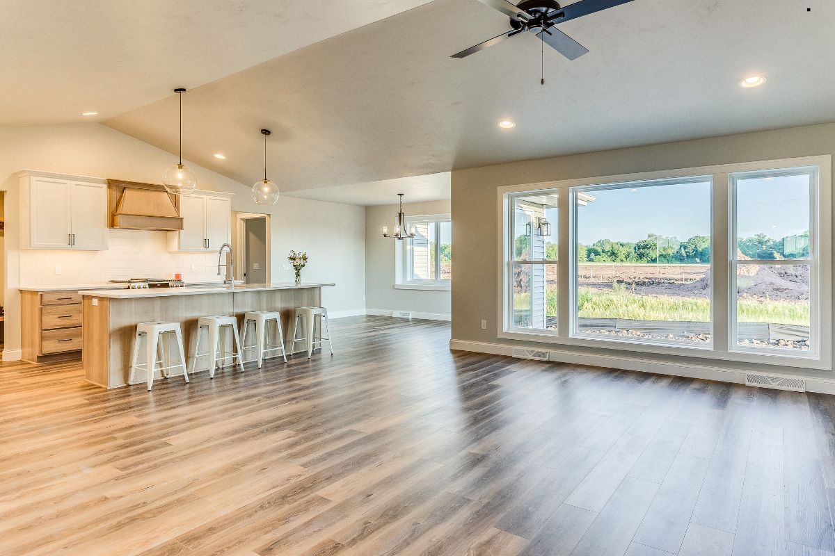 Spacious modern open-concept living area featuring a light wood kitchen island, bar stools, and large windows with a scenic view.